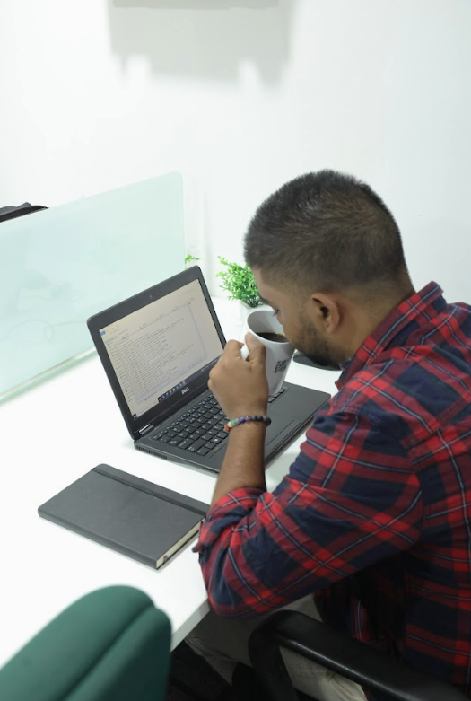 Close-up of a workstation with laptop, notebook, charging points, comfortable chair, and coffee mug